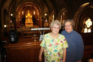 Sisters Alice Simon, left, and RoseMarie Reuer have celebrated family and community milestones in St. Anthony of Padua Catholic Church for six generations. They and deceased sister Agnes Reuer have proudly hosted numerous tours of the “Cathedral on the Prairie.” By Wendy Roston/Dakotafire Media